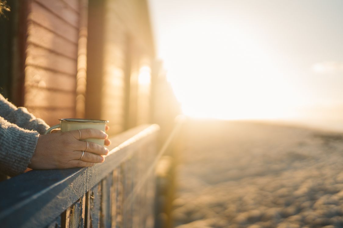 Hand holding a warm mug at sunrise — calm and hopeful